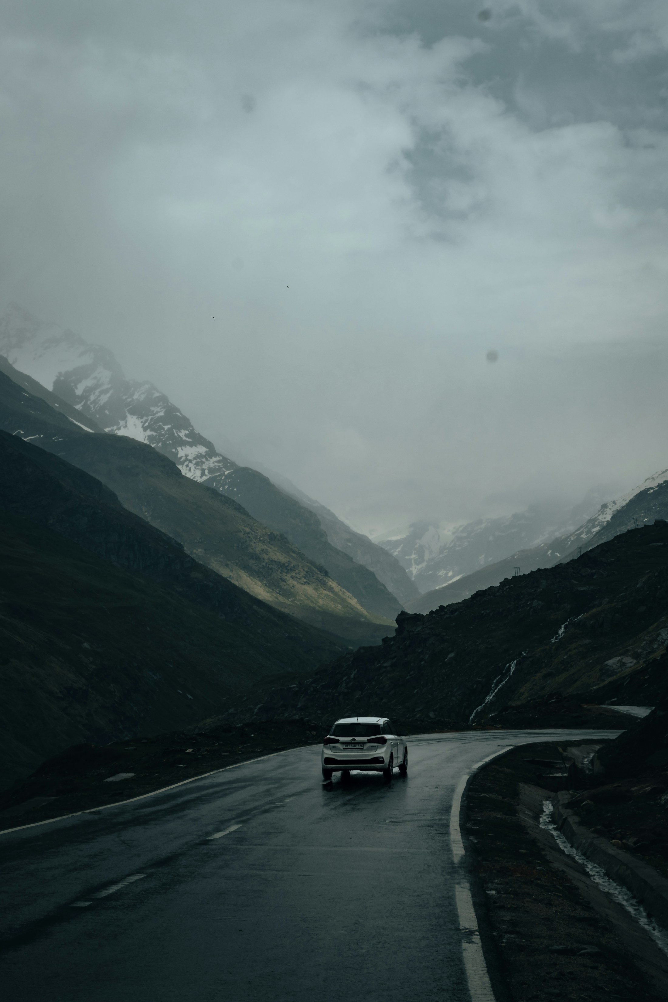 A white sports car following a wet mountain road beneath low clouds
