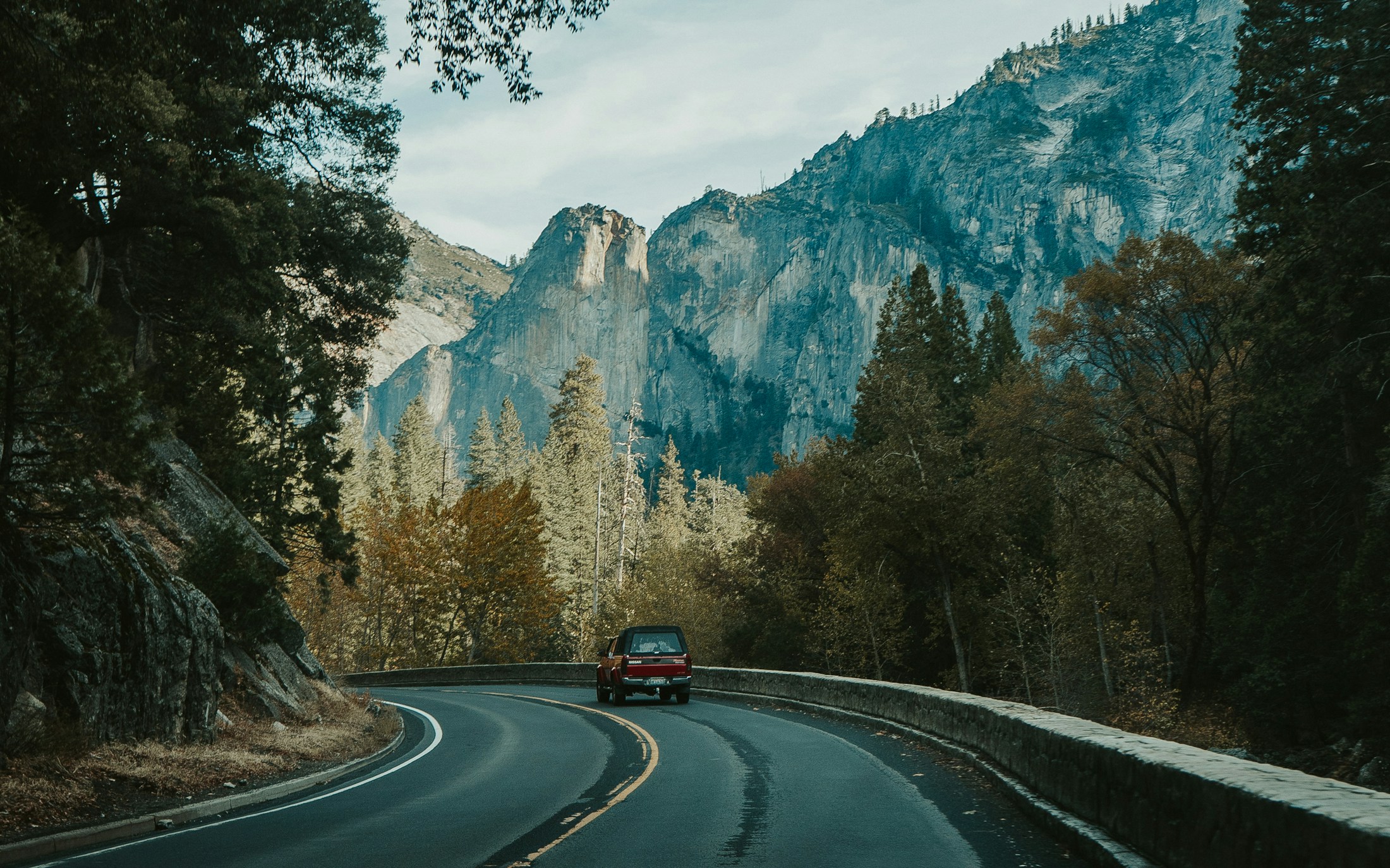 A car travelling along a broad mountain road in changing weather